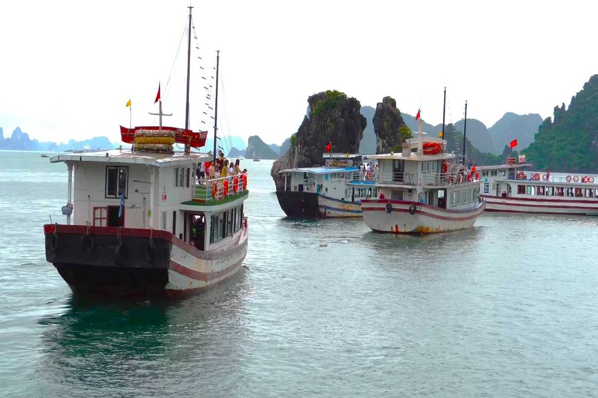 Traditional tour boat cruising close to Fighting Cocks Islet Halong Bay limestone rocks