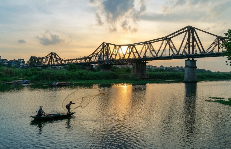 Fishermen Casting Nets Under Long Bien Bridge at Sunset Fishermen casting nets under Long Bien Bridge at sunset with the golden sky reflecting on the Red River in Hanoi.