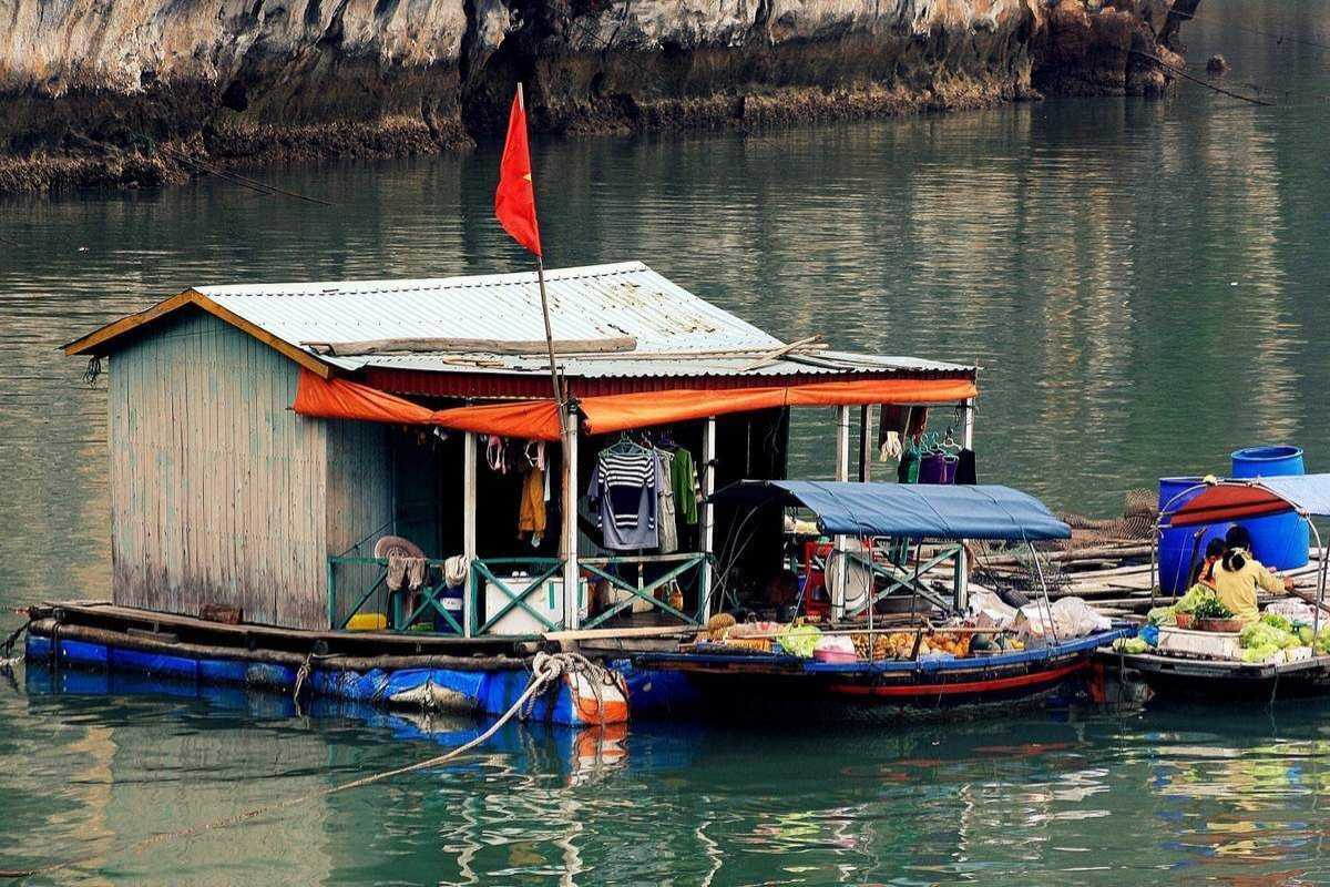 Wide shot of Cong Dam Fishing Village with fishing boats and limestone cliffs in Bai Tu Long Bay