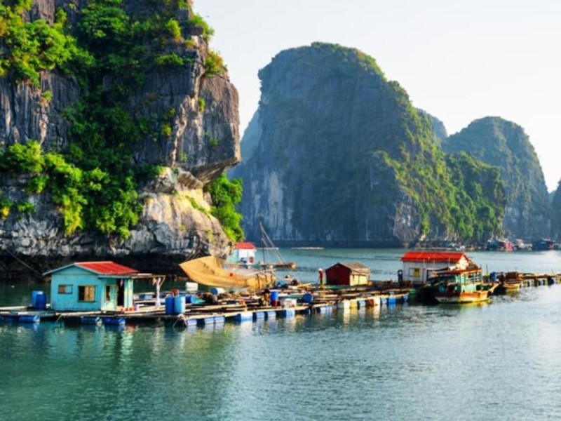 floating-village-halong-bay-titov-island.jpg A floating fishing village in Halong Bay, with limestone cliffs and green trees, capturing the essence of Titov Island and surrounding areas.
