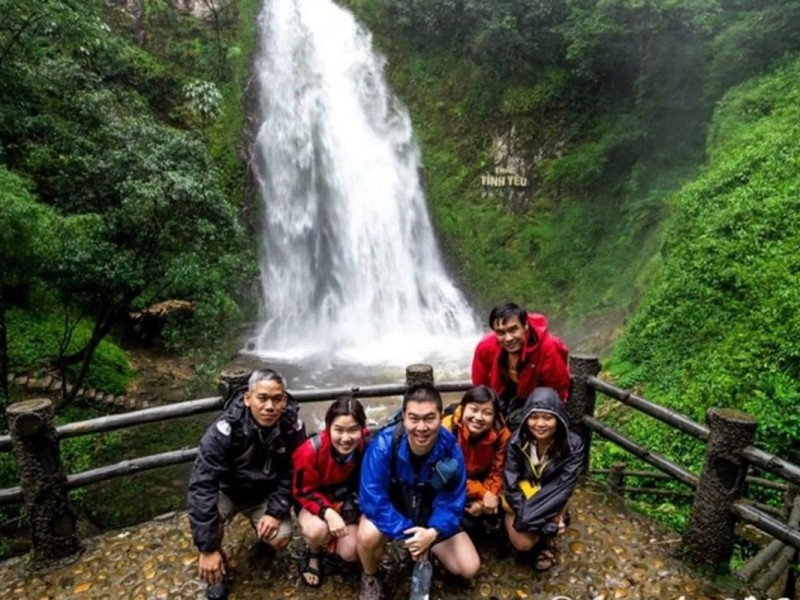 Group of tourists smiling in front of Love Waterfall in Sapa, surrounded by lush greenery
