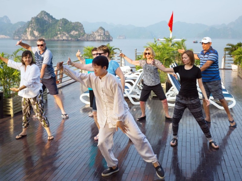 Group Tai Chi Practice on a Luxury Cruise A group practicing Tai Chi on a luxury cruise deck in Halong Bay, set against scenic waters.