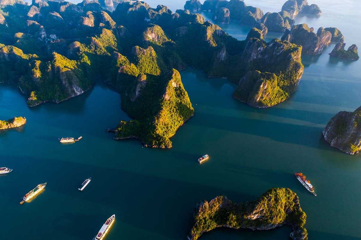 A cruise ship sailing through emerald waters surrounded by towering limestone karsts in Ha Long Bay.