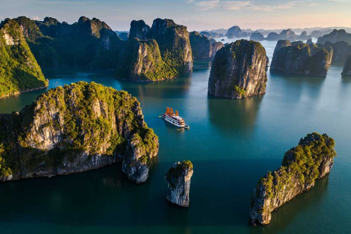 Limestone islands covered in greenery with cruise boats navigating the calm waters of Ha Long Bay.