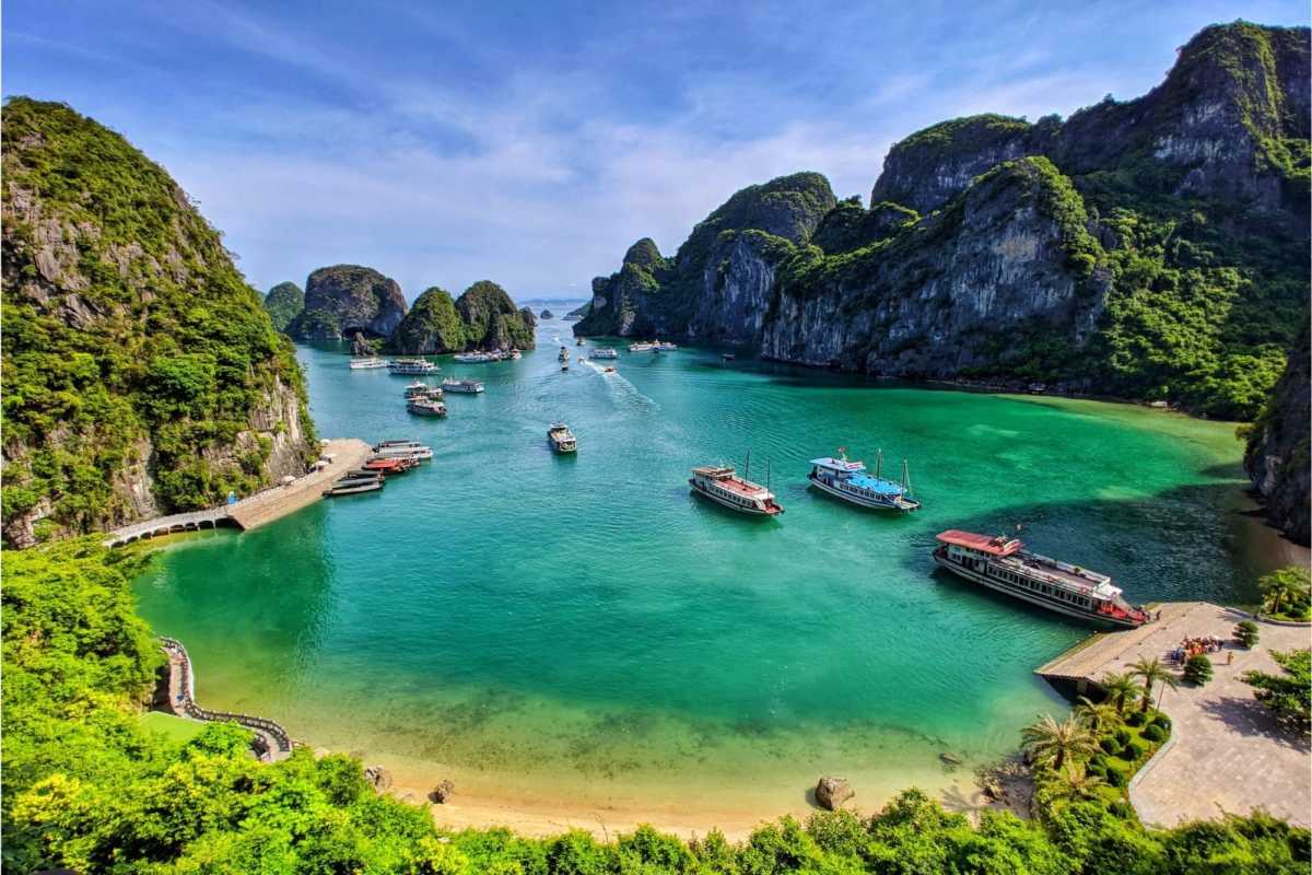 Limestone islands in Ha Long Bay bathed in soft early morning light with calm waters and boats navigating the bay.