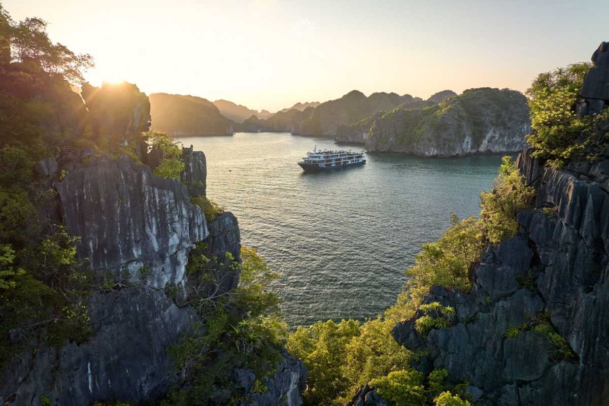 Panoramic aerial view of Ha Long Bay featuring towering limestone formations surrounded by turquoise water and boats.