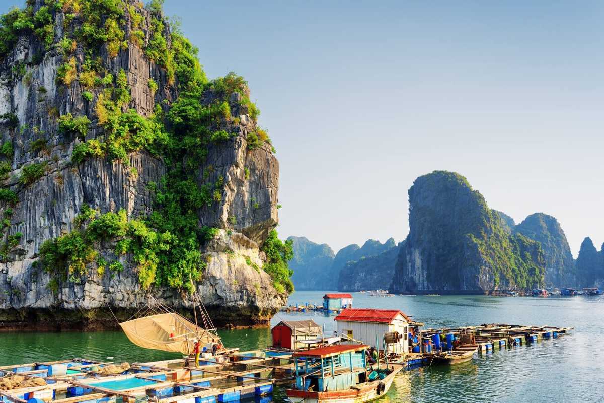 Limestone islands silhouetted against a colorful sunset sky over calm waters in Ha Long Bay.