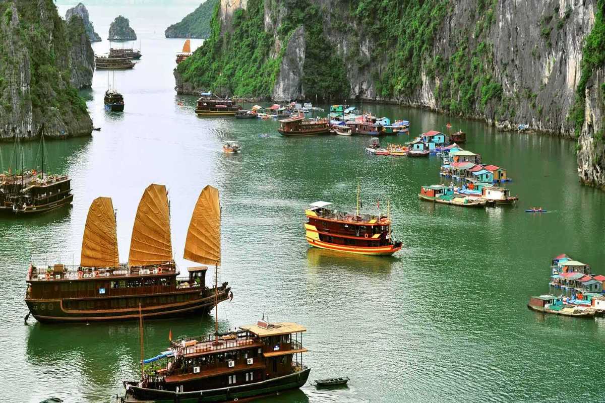 Traditional wooden junk boats near a floating fishing village surrounded by towering limestone karsts in Ha Long Bay.