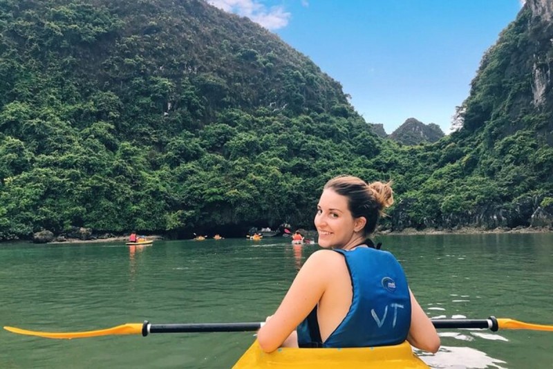 halong-bay-kayaking-titov-island.jpg A woman kayaking in Halong Bay with lush green hills and limestone cliffs in the background, near Titov Island.