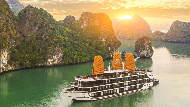 halong-bay-overnight-cruise-titov-island.jpg A luxurious overnight cruise boat sails through Halong Bay at sunset, with the towering cliffs of Titov Island in the distance.