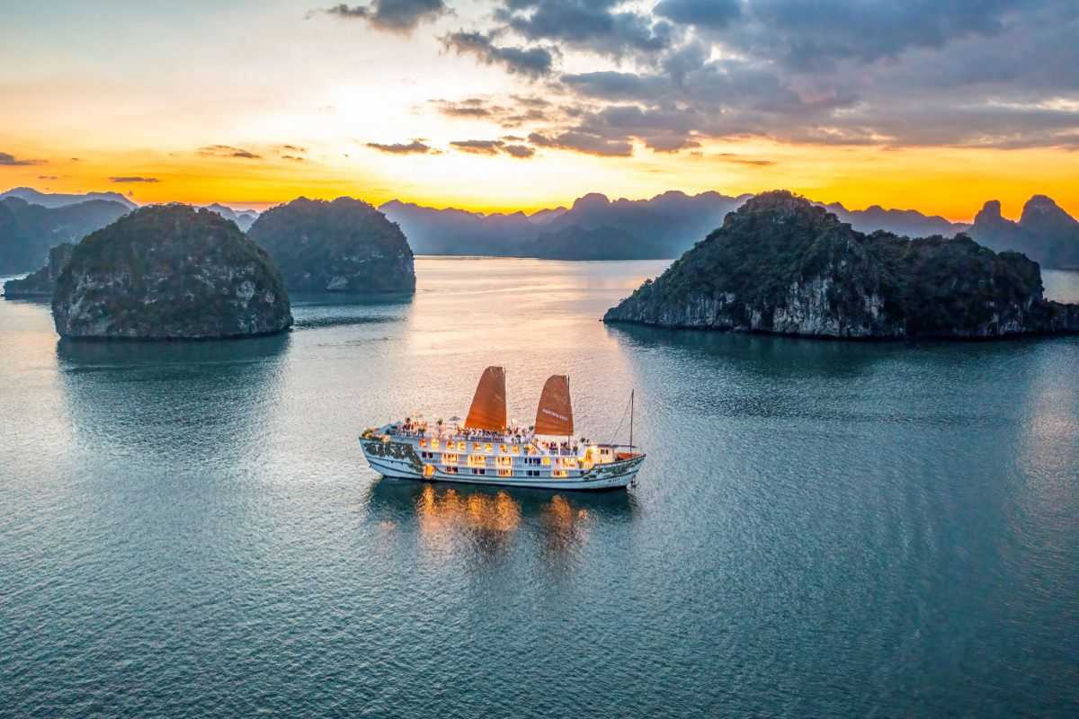 A calm Halong Bay scene with a modern cruise ship passing between emerald cliffs under a setting sun.