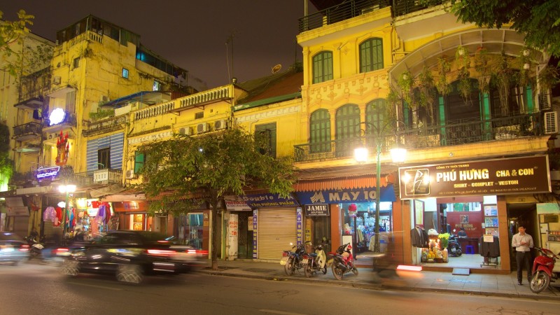The vibrant streets of Hanoi French Quarter at night, featuring colonial buildings with yellow facades, street shops, and traffic.