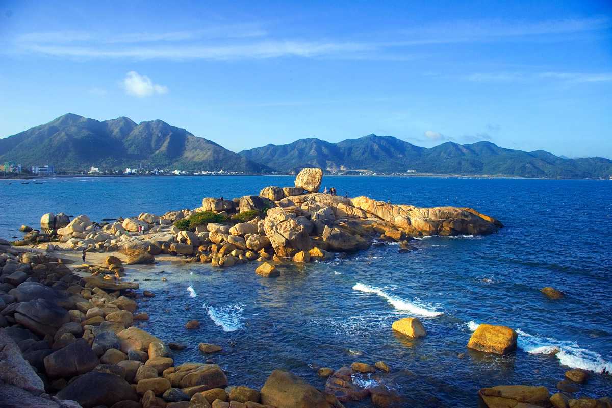 Hon Mieu Island coastal rock formations with Nha Trang mountains Natural coastal rock formations on Hon Mieu Island with clear blue skies and Nha Trang mountains in the background.