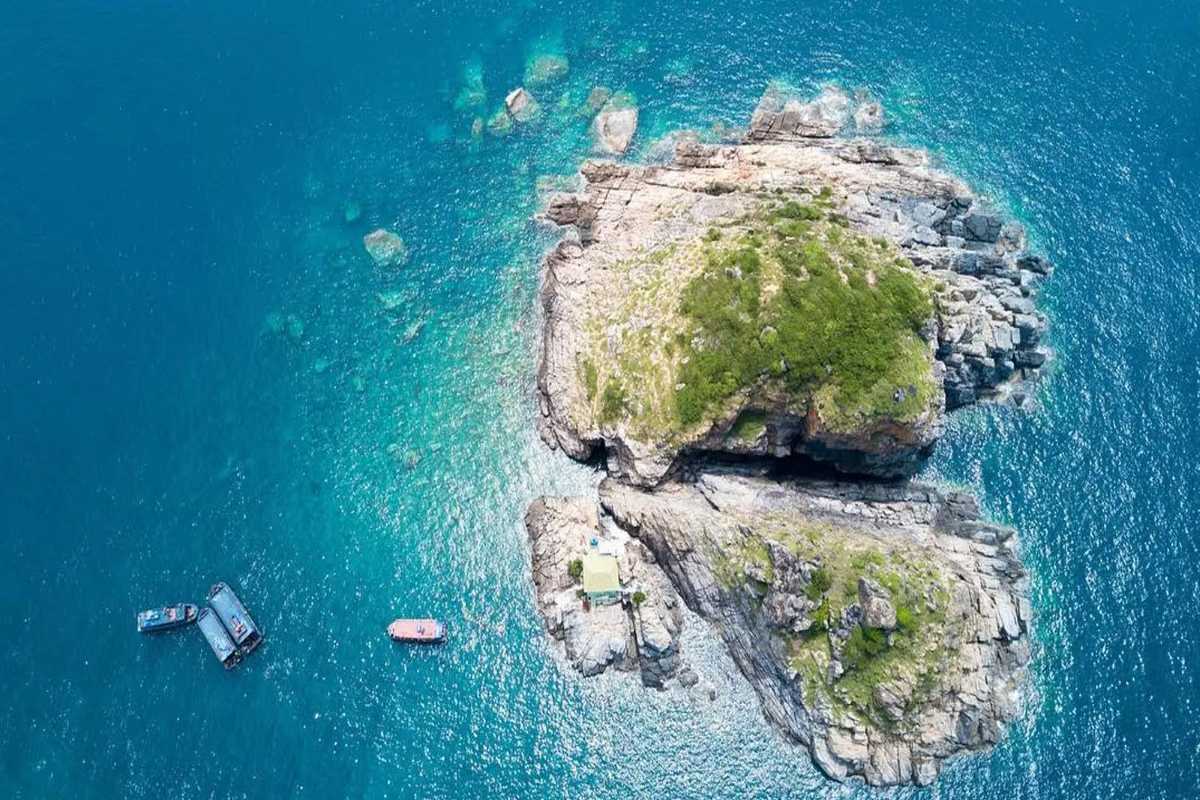 Top-down view of rocky cliff formations and boats anchored offshore near Hon Mot Island