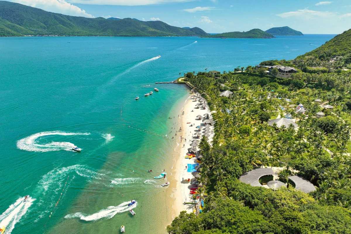 Visitors enjoying beach activities along the shoreline of Hon Mun Island’s resort with lush green hills behind.