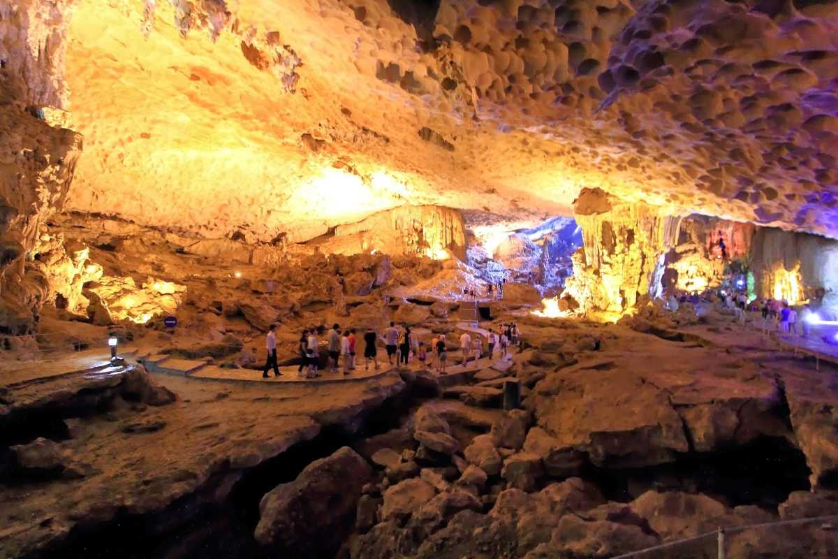 Colorful illuminated rock formations inside Sung Sot Cave Halong Bay with tourists walking along the paved path