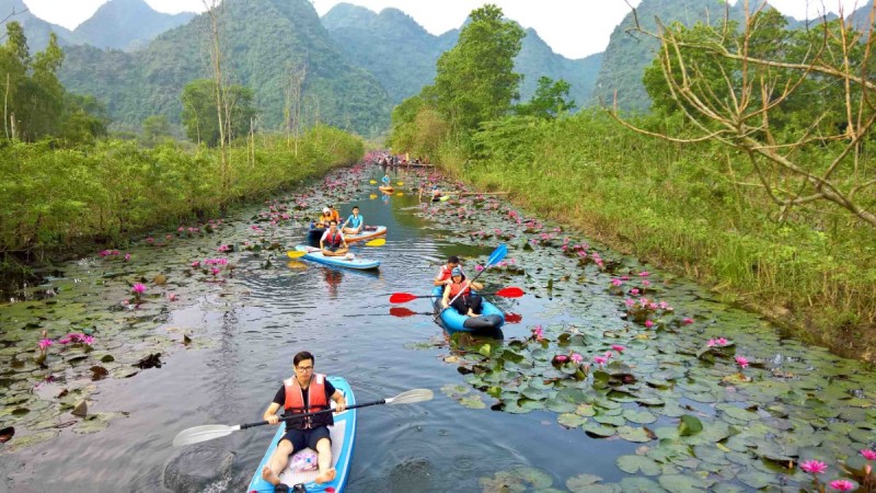 Kayaking Along Yen Stream at Perfume Pagoda – A Unique Adventure Tourists kayaking on Yen Stream at Perfume Pagoda surrounded by water lilies and picturesque mountain views.