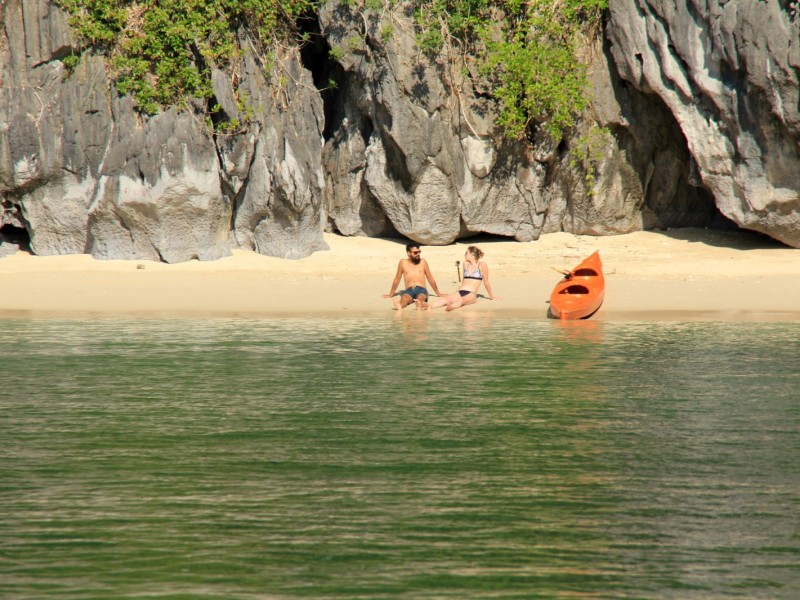 A couple relaxing on the beach with a kayak at Ba Trai Dao Islet in Halong Bay.
