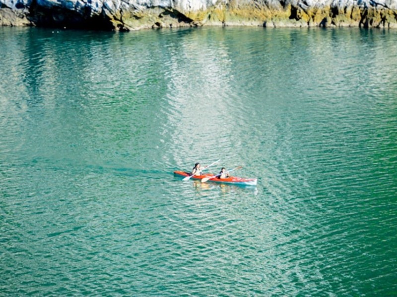 Kayaking at Ba Ham Lake in Lan Ha Bay Two kayakers paddling through the tranquil waters of Ba Ham Lake in Lan Ha Bay, surrounded by limestone cliffs.
