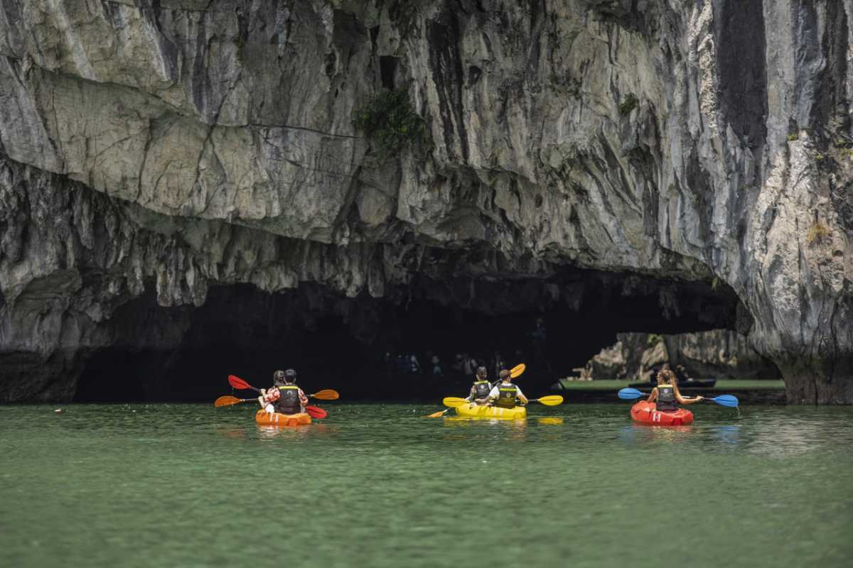 Colorful kayaks entering the natural limestone tunnel of Luon Cave with lush greenery above