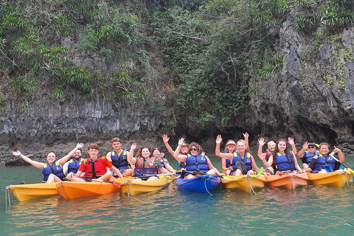 Group of kayakers smiling and waving near Luon Cave with cliffs in the background