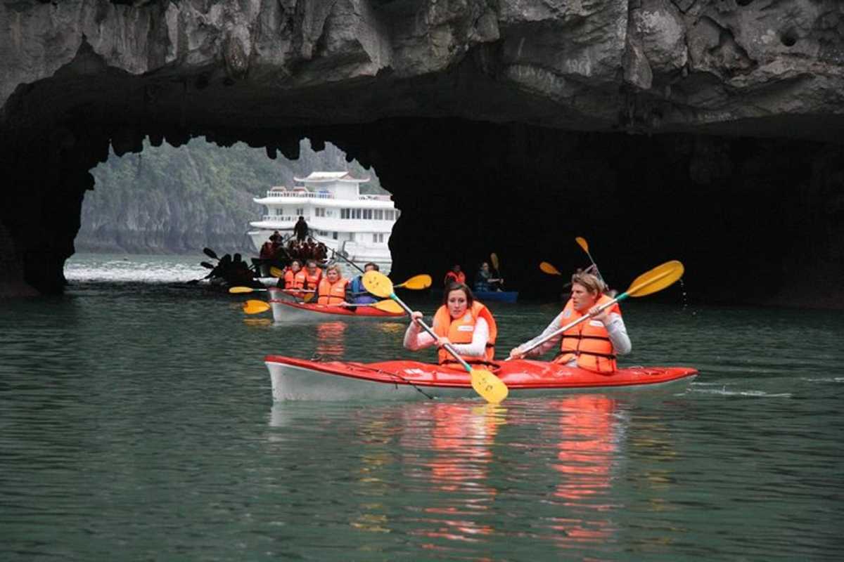 Multiple kayaks paddling together near the entrance of Luon Cave surrounded by lush vegetation