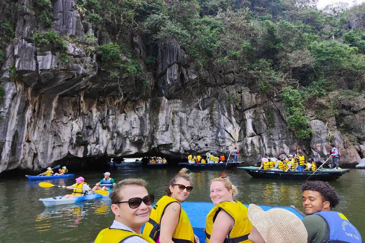 Kayakers and traditional bamboo boats sharing the water near Luon Cave limestone cliffs