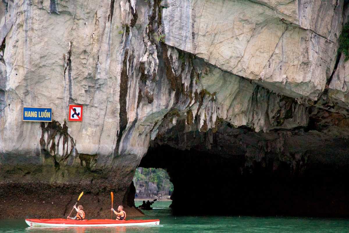 Kayakers paddling under a rugged limestone archway at Luon Cave in Halong Bay