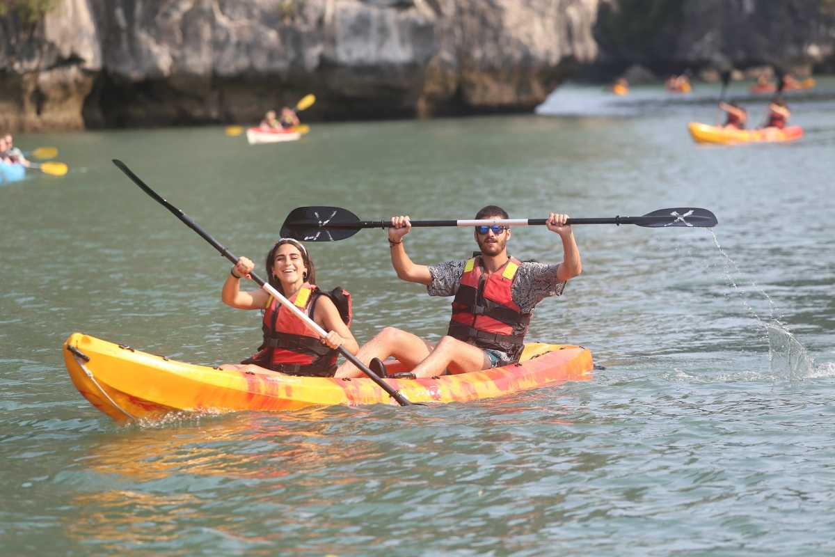 Kayakers paddling amidst lush green vegetation and limestone cliffs in Luon Cave Halong Bay