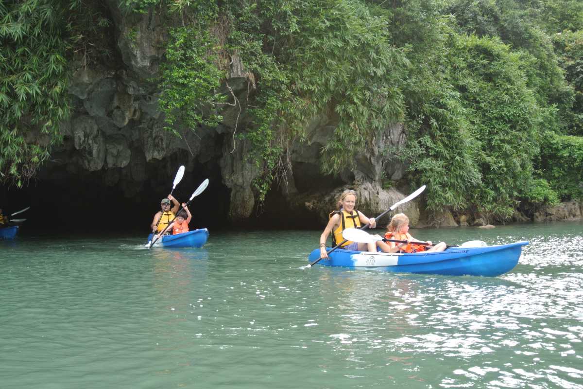 Mixed group kayaking in colorful kayaks near limestone cliffs at Luon Cave Halong Bay