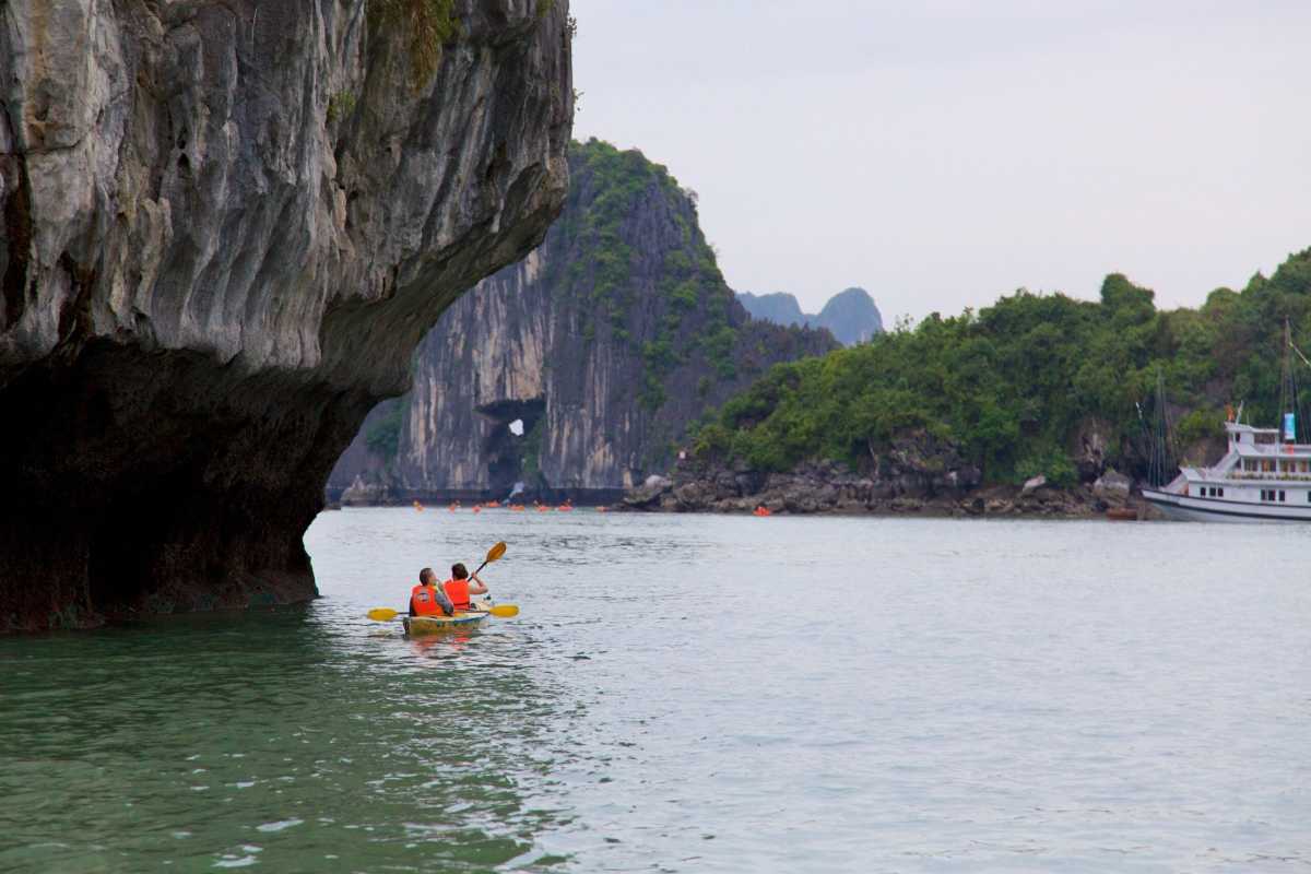 Kayaks on calm water surrounded by towering limestone karsts and a boat in the distance