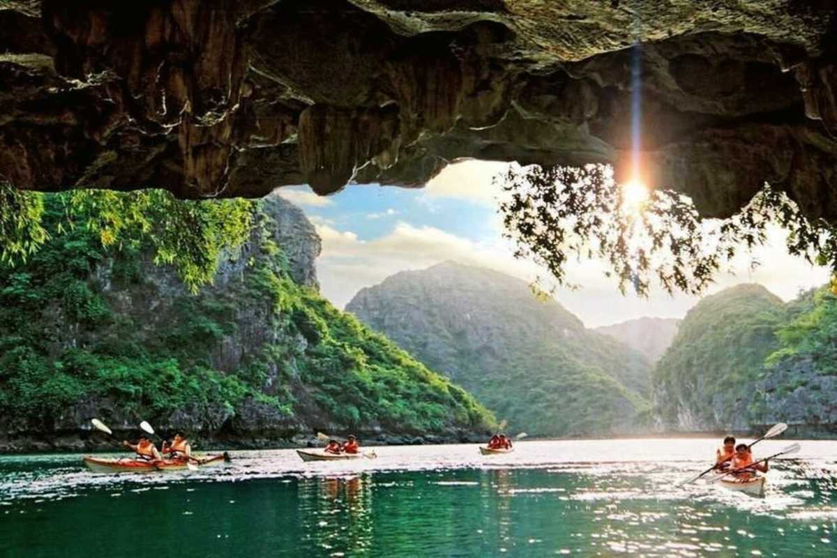 Kayakers paddling calmly on emerald water near Luon Cave entrance framed by limestone cliffs