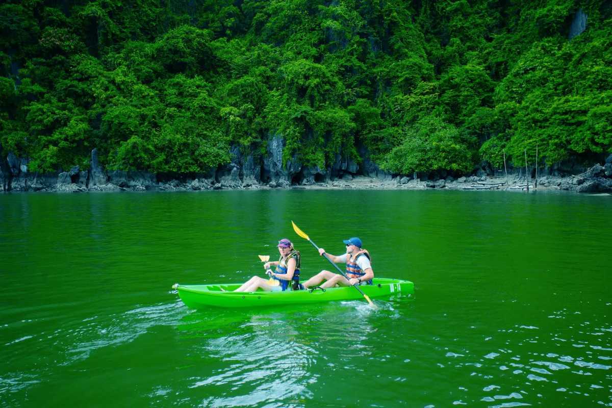 Kayaker entering shadowed cave opening surrounded by limestone in Luon Cave Halong Bay