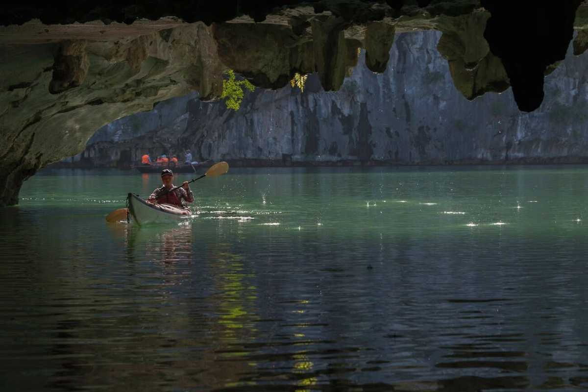 Solo kayaker paddling inside Luon Cave with sunlight filtering through limestone formations