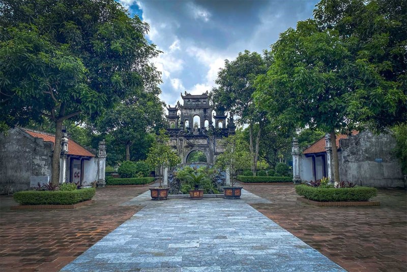Le Mat Snake Village Courtyard and Gate The serene courtyard of Le Mat Snake Village, leading to the ancient stone gate surrounded by lush trees and traditional buildings, reflecting the village's peaceful atmosphere and cultural heritage.