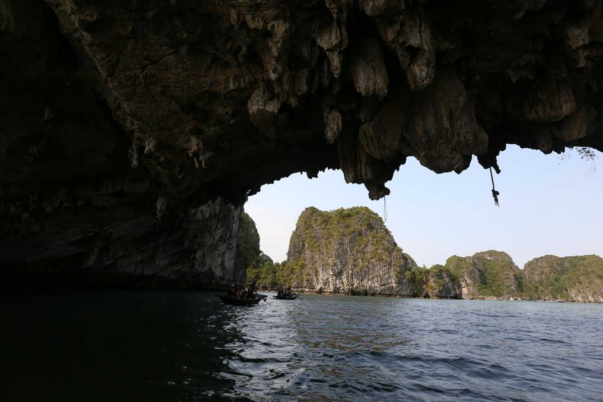Group tour boats entering the limestone cave entrance at Luon Cave, Halong Bay