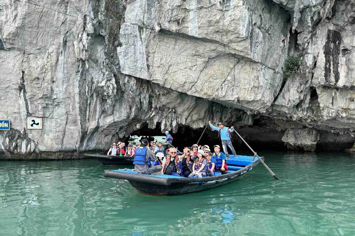 Kayakers paddling towards the limestone cave entrance of Luon Cave, Halong Bay