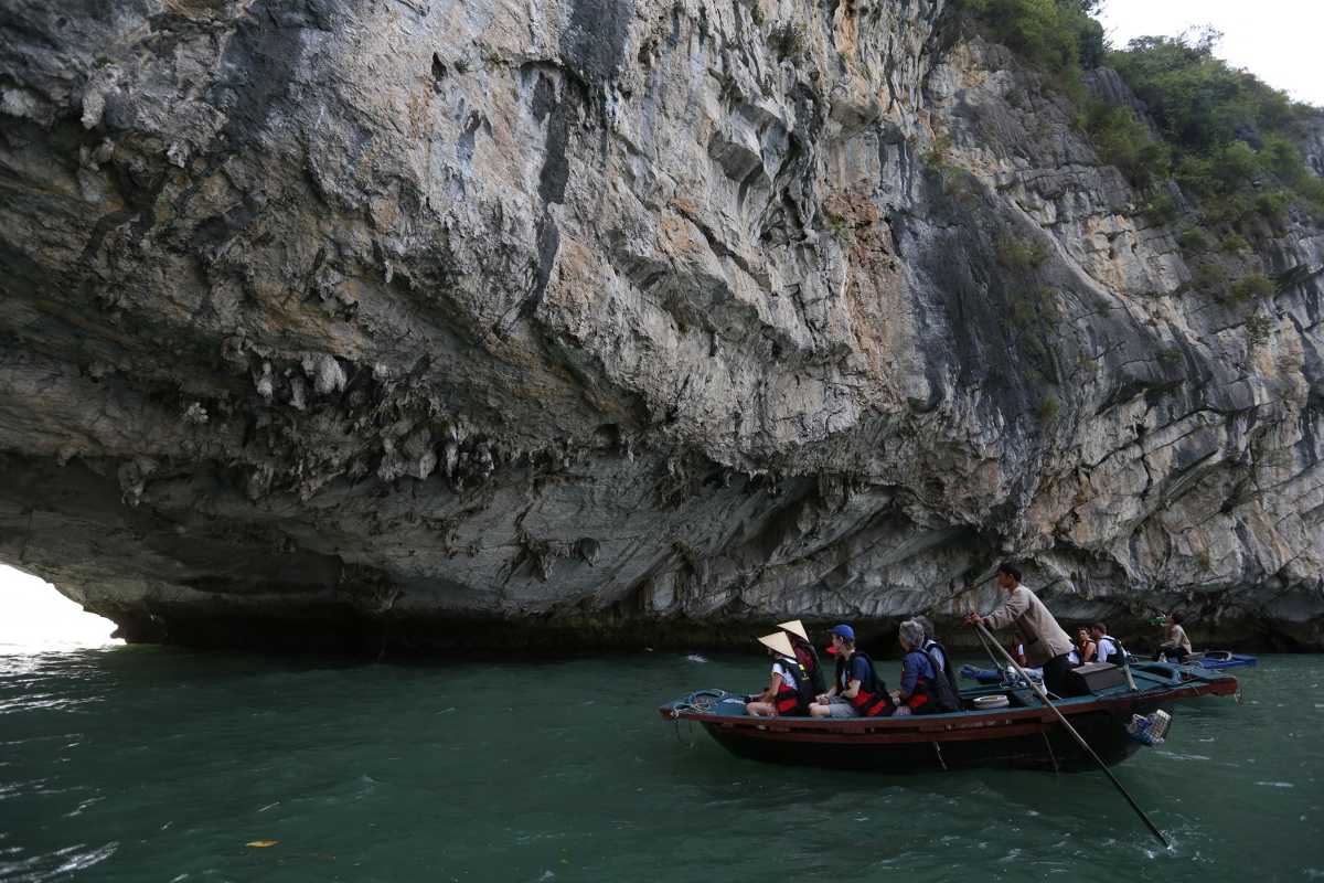 Kayakers and boats passing under limestone archway at Luon Cave, Halong Bay