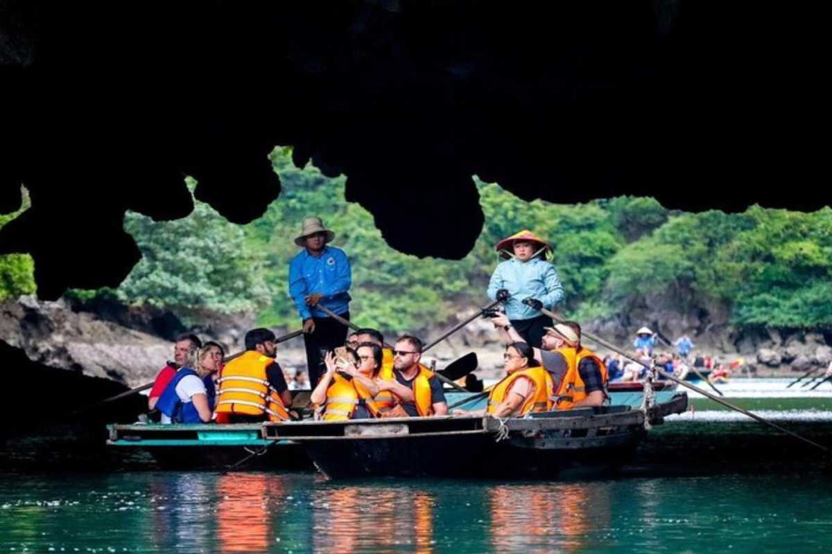 Tourists on boat entering Luon Cave in Halong Bay surrounded by limestone cliffs and green water