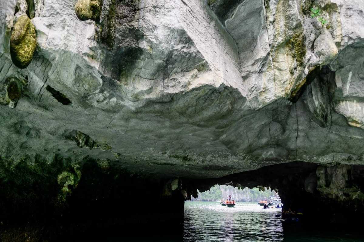 Tour boat and kayakers near limestone cave entrance of Luon Cave, Halong Bay