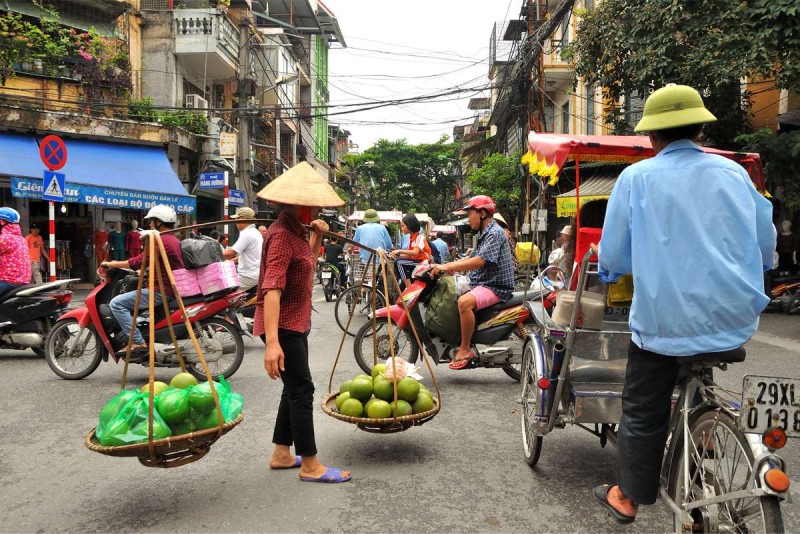 Morning Market Scene in Hanoi French Quarter A bustling morning market scene in Hanoi French Quarter, with vendors carrying fruits and goods on traditional shoulder baskets.