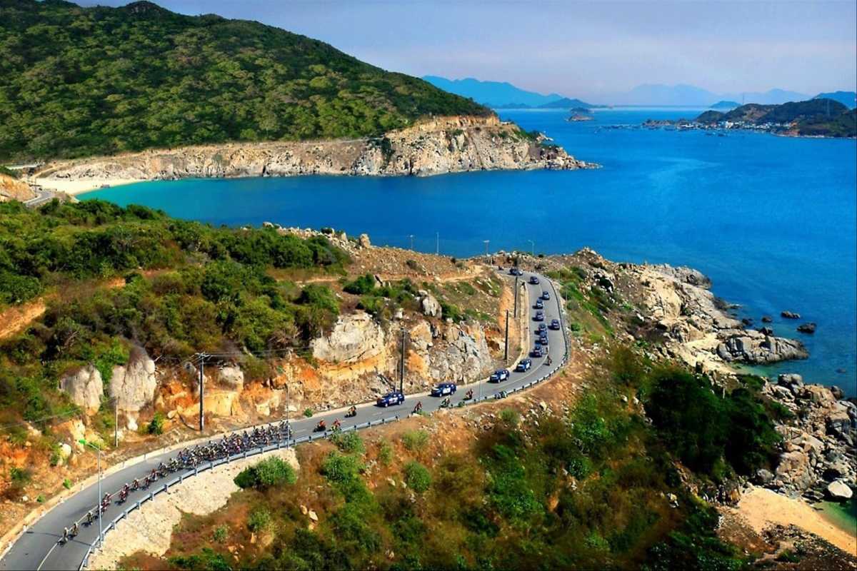Scenic coastal road overlooking Nha Phu Bay waters A winding coastal road with motorcycles and vehicles offering stunning views over Nha Phu Bay’s turquoise waters and green hills near Nha Trang.