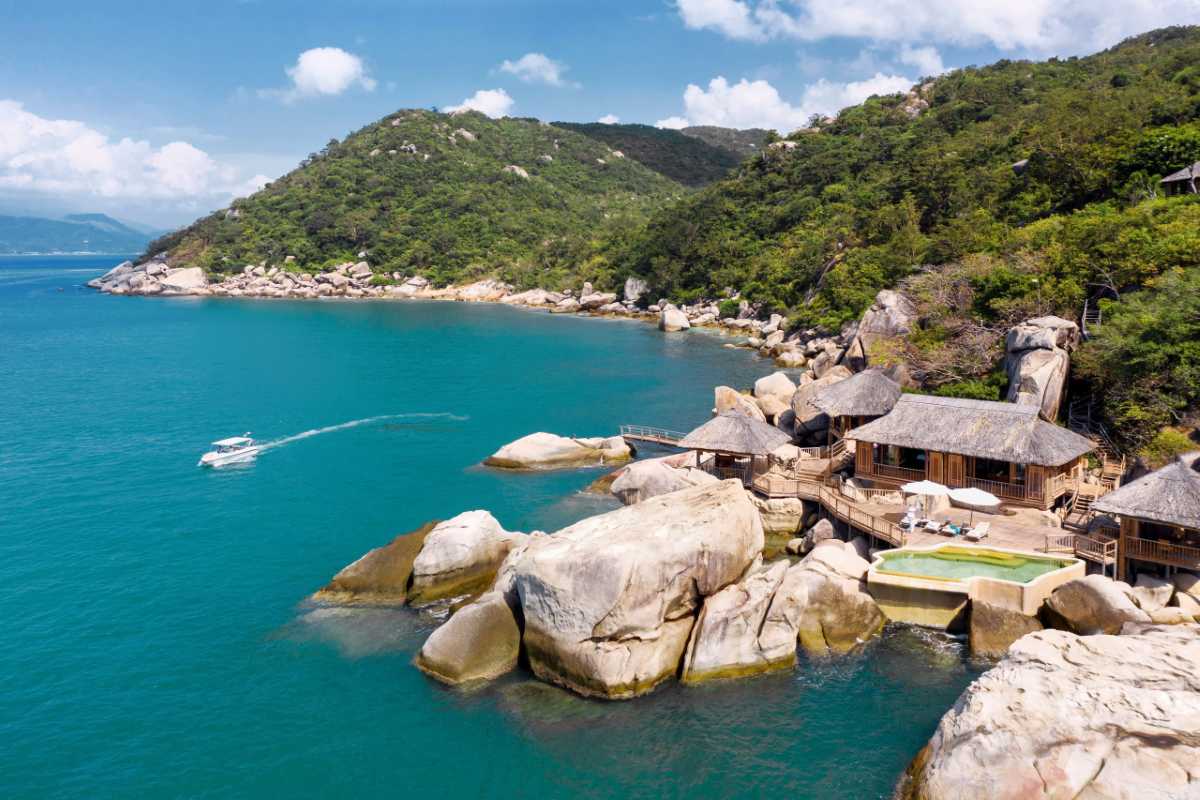 Coastal villa escape Ninh Van Bay Stone villas on rocky shoreline with forested hills and speedboat in the water.
