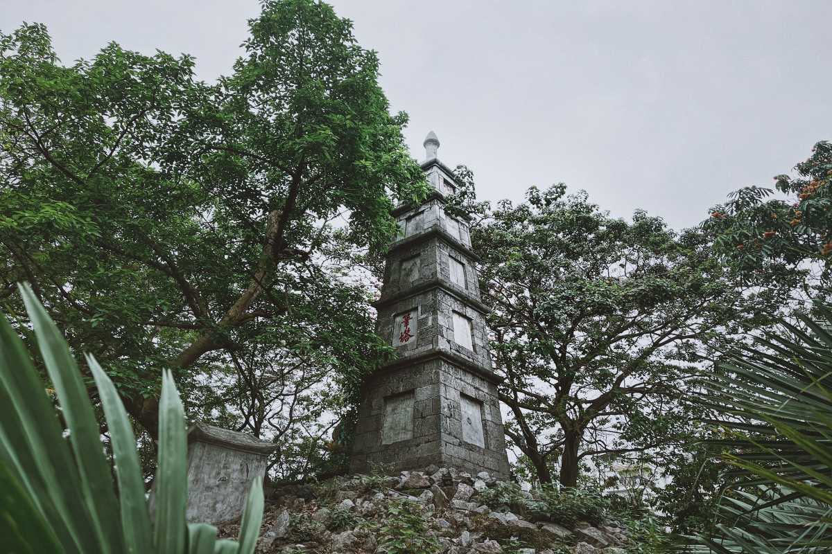 Pen Tower rising above lush trees and rocky base at Hoan Kiem Lake in Hanoi