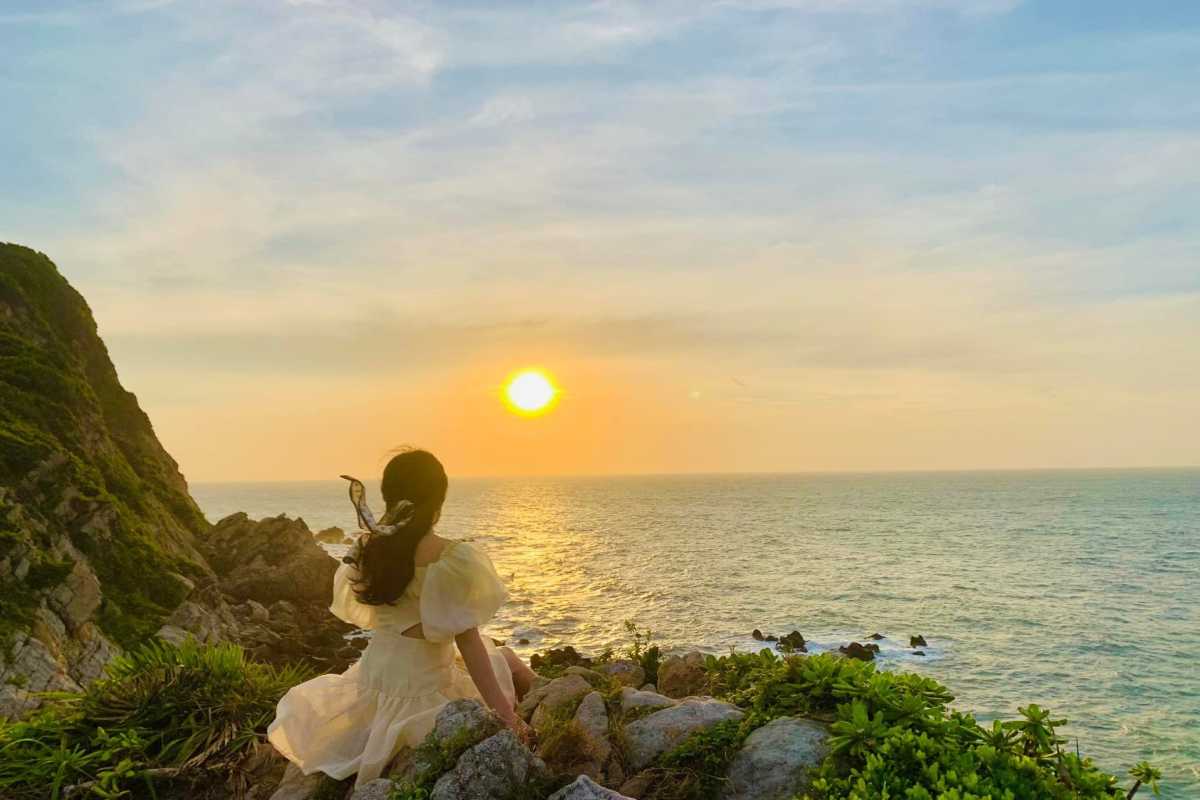 Woman enjoying the sunset view over rocky coastline on Quan Lan Island