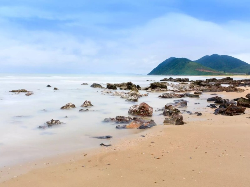 Rugged shoreline with rocks along Quan Lan Island’s beach.