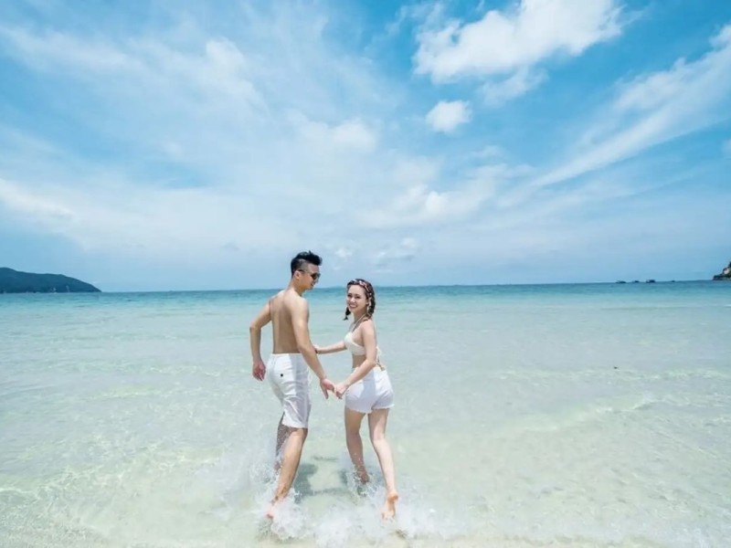 Couple holding hands while walking along the clear waters of Quan Lan Island’s beach.