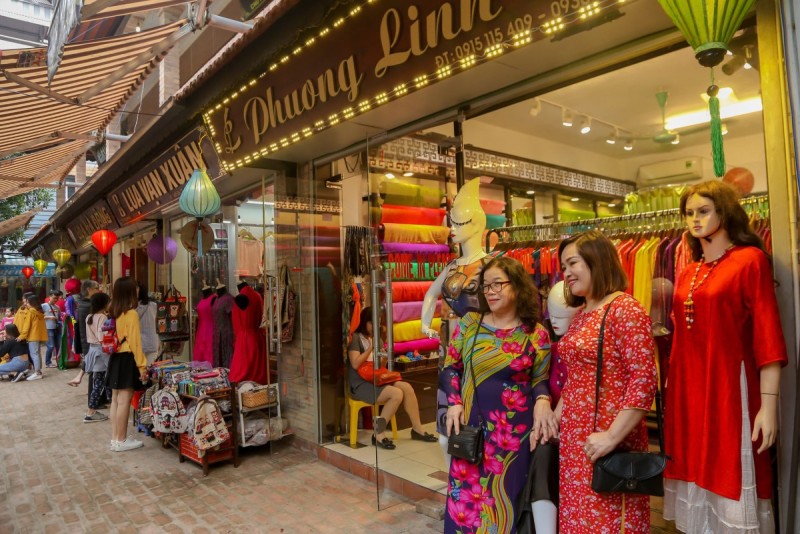 Shopping at Van Phuc Silk Stalls in Hanoi Tourists shopping at Van Phuc Silk Village stalls with a variety of silk fabrics and clothing on display.