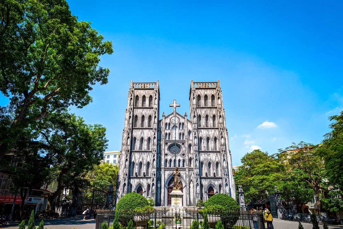 Facade of St. Joseph’s Cathedral Hanoi with twin bell towers and a large cross under a clear blue sky