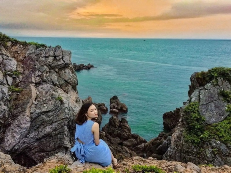 Woman sitting on a cliff overlooking the ocean at sunset on Quan Lan Island.